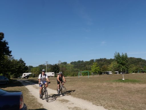 Deux cyclistes sur un chemin, paysage verdoyant et ciel bleu en arrière-plan.