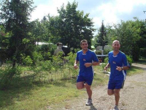 Deux coureurs en tenue de sport bleue joggent sur un chemin entouré d'arbres.